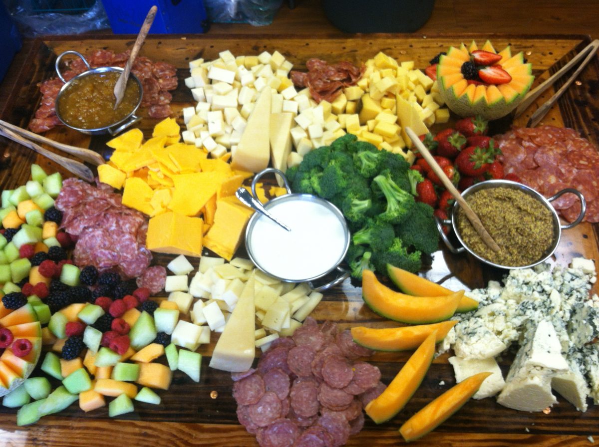 Large grazing board of cheeses, salami, melon, berries and broccoli with dips