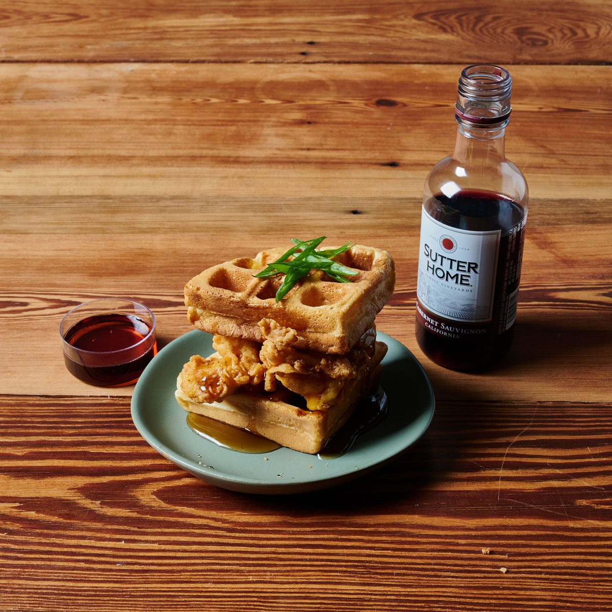 Fried chicken and waffles with syrup and scallions beside a mini bottle of Cabernet Sauvignon