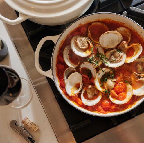 Clams in tomato broth with herbs in a white braiser on a stovetop