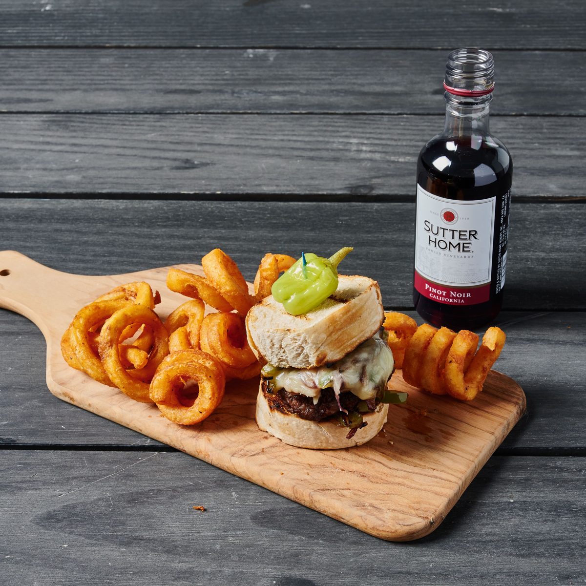 Burger with melted cheese and a pepperoncini, curly fries and a mini bottle of Pinot Noir