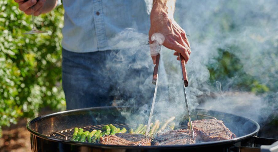 Steaks and asparagus on a smoking charcoal grill, turned with tongs