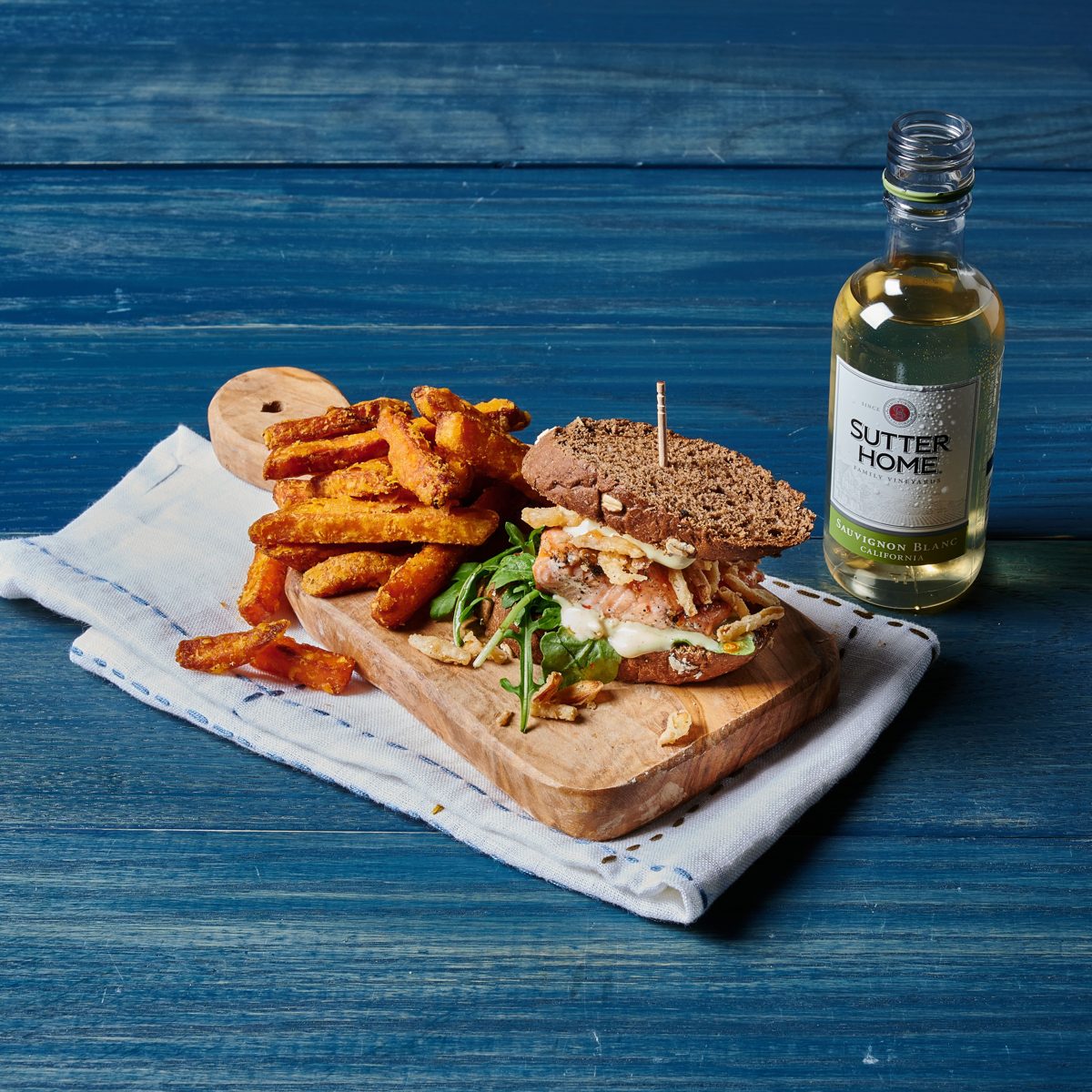 Salmon sandwich on dark bread with arugula and crispy onions, sweet potato fries and a mini bottle of Sauvignon Blanc